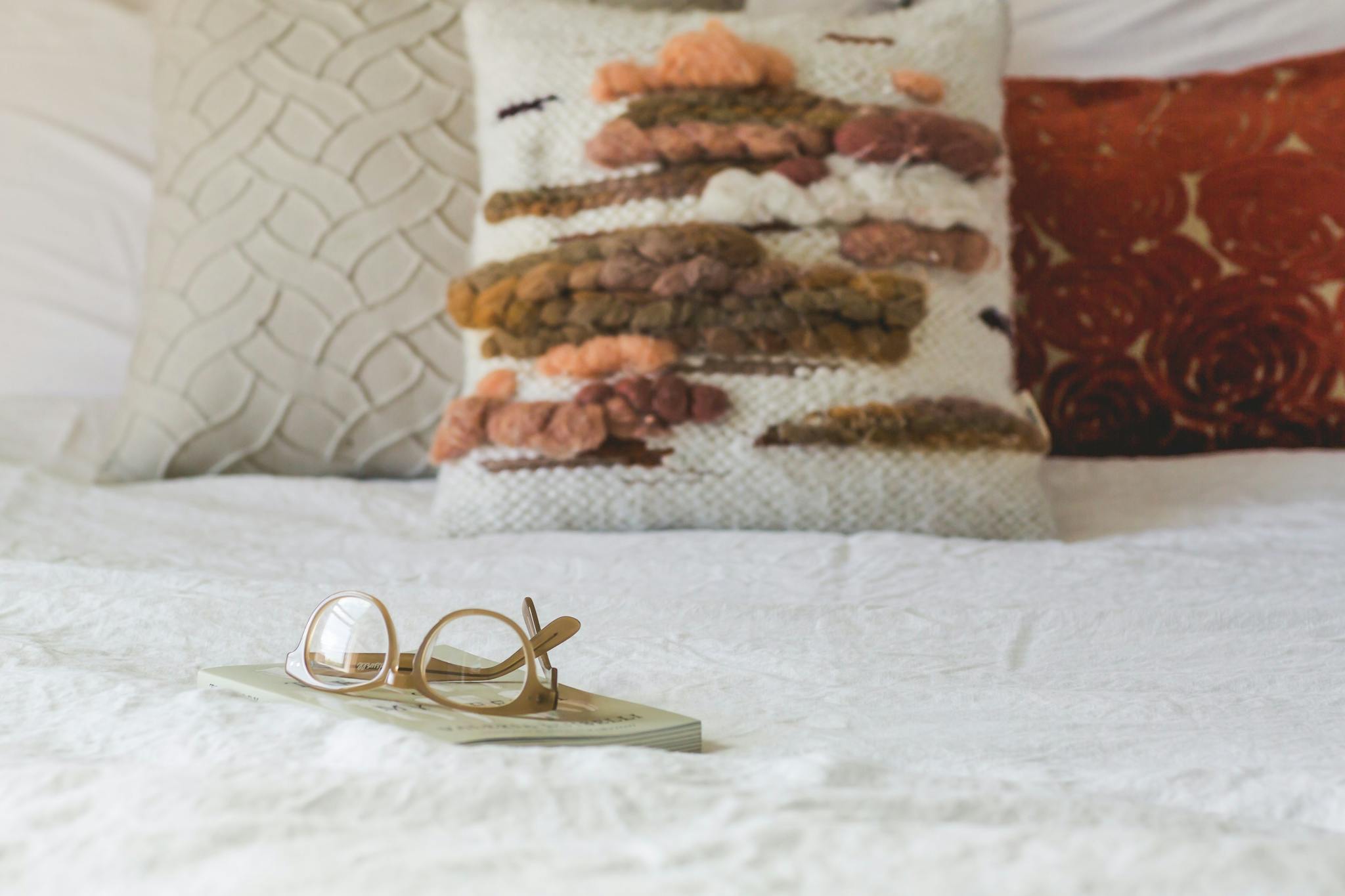 A stylish bedroom featuring artistic throw pillows and eyeglasses placed on a book, offering a cozy ambiance.