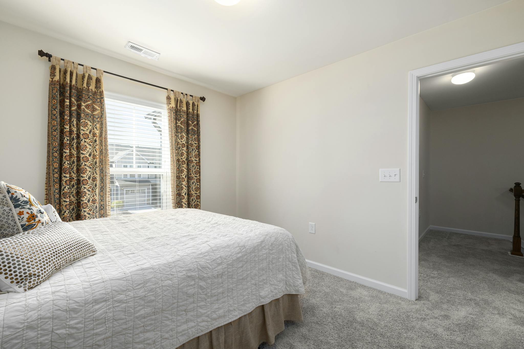 Bright minimalist bedroom interior with a neatly made bed and patterned curtains.