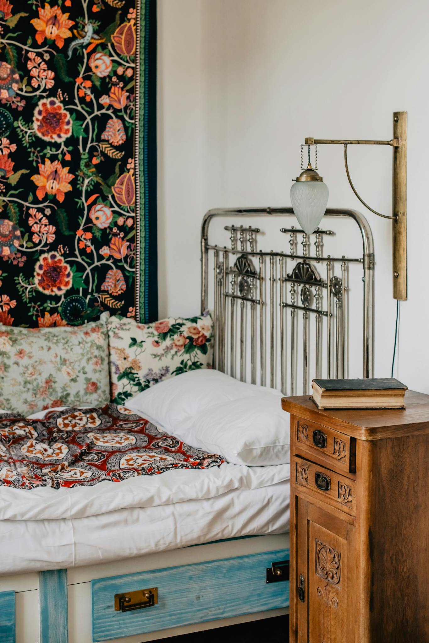 Cozy vintage bedroom featuring floral decor, antique iron bedframe, and wooden nightstand.