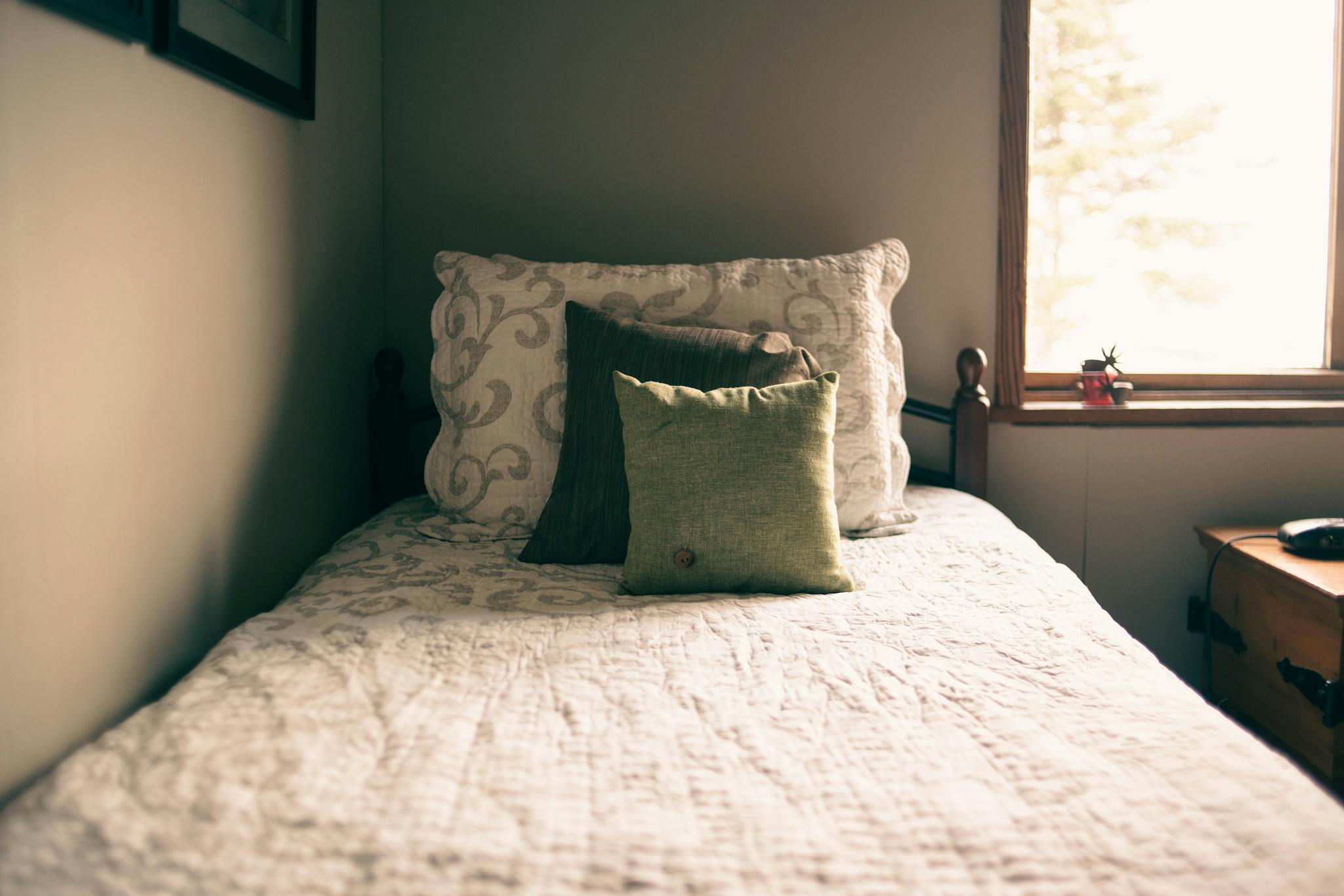 Inviting bedroom with a sunlit window and decorative pillows on a quilted bed.
